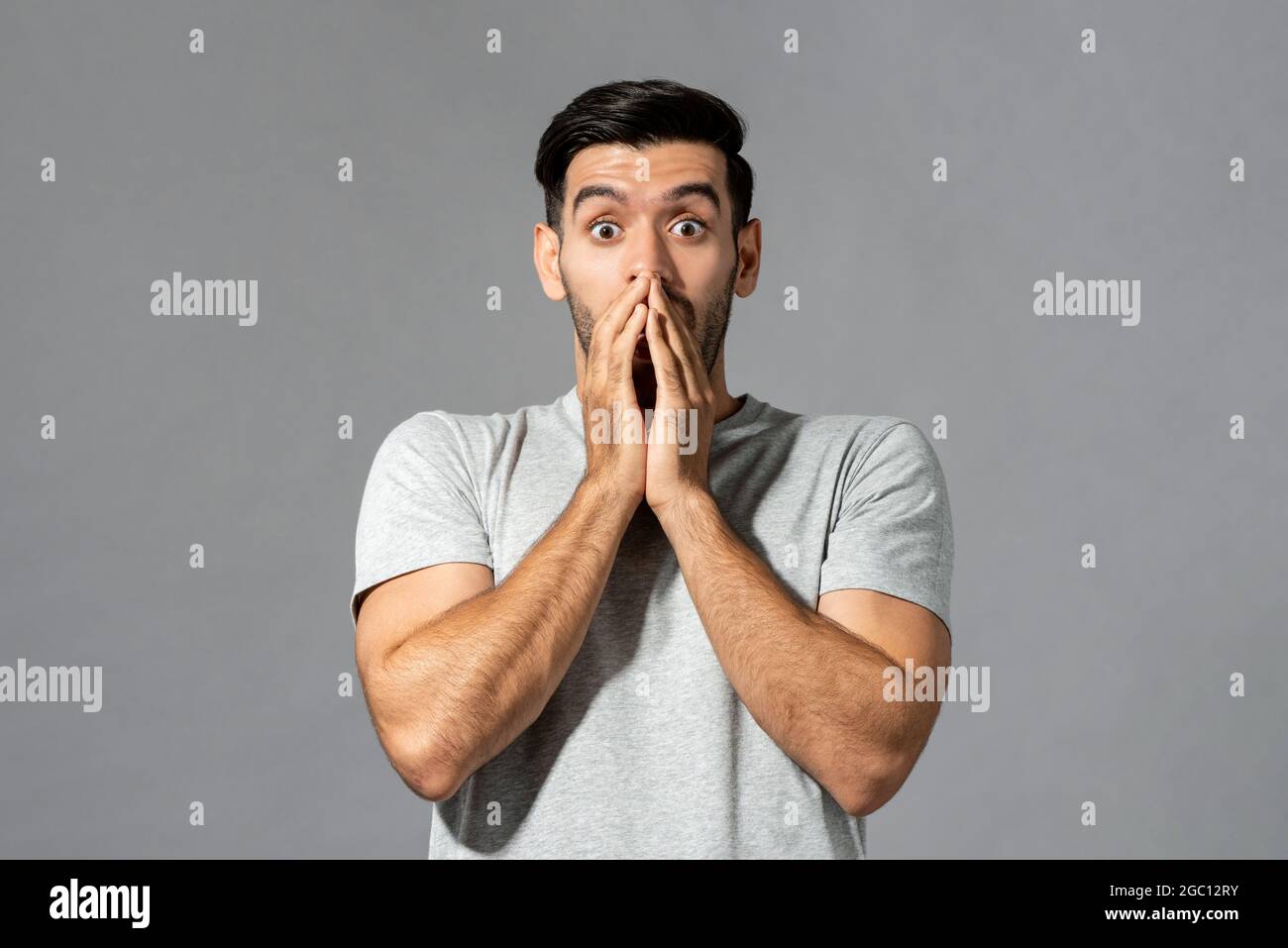 hk``````````````````````````````````````````````````````Shocked young Caucasian man with hands covering mouth in isolated light gray studio background Stock Photo